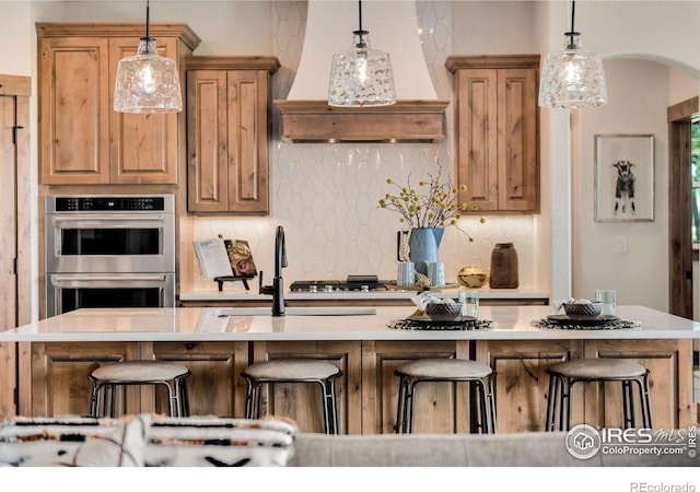 kitchen featuring a kitchen island with sink, backsplash, a breakfast bar area, and premium range hood