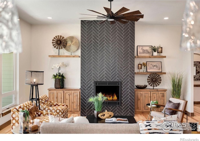 living room with a fireplace, light wood-type flooring, and ceiling fan