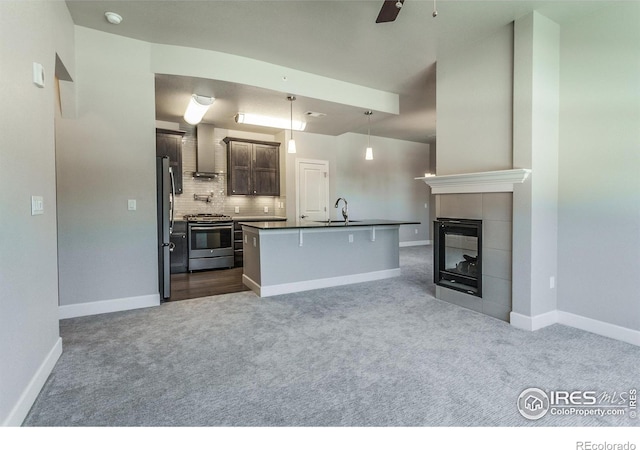 kitchen with wall chimney exhaust hood, a kitchen island with sink, hanging light fixtures, stainless steel appliances, and decorative backsplash