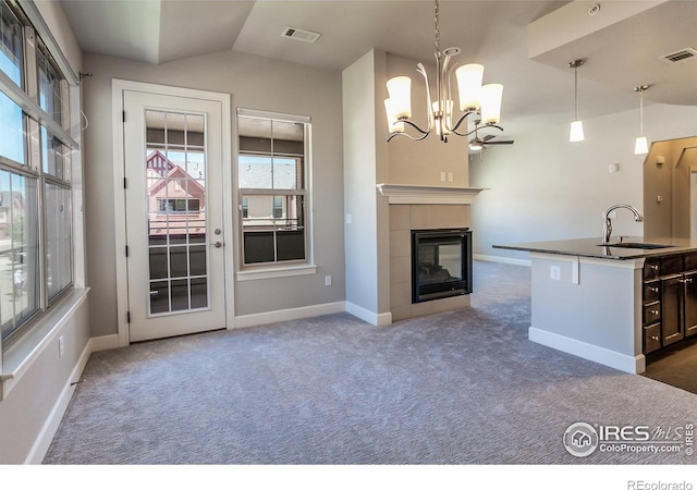 kitchen with a kitchen island with sink, sink, a tile fireplace, hanging light fixtures, and lofted ceiling