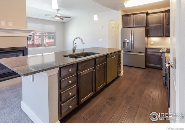 kitchen featuring sink, backsplash, dark stone counters, a center island with sink, and appliances with stainless steel finishes