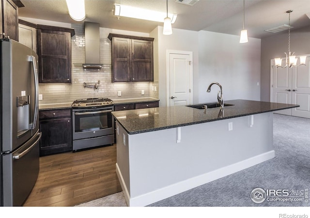 kitchen with sink, wall chimney exhaust hood, a kitchen breakfast bar, a center island with sink, and appliances with stainless steel finishes