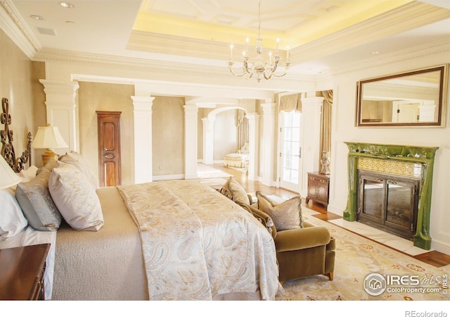 bedroom with a fireplace, a raised ceiling, a chandelier, decorative columns, and crown molding