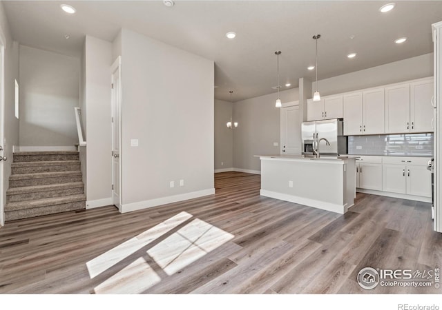 kitchen with an island with sink, white cabinets, pendant lighting, and light hardwood / wood-style flooring