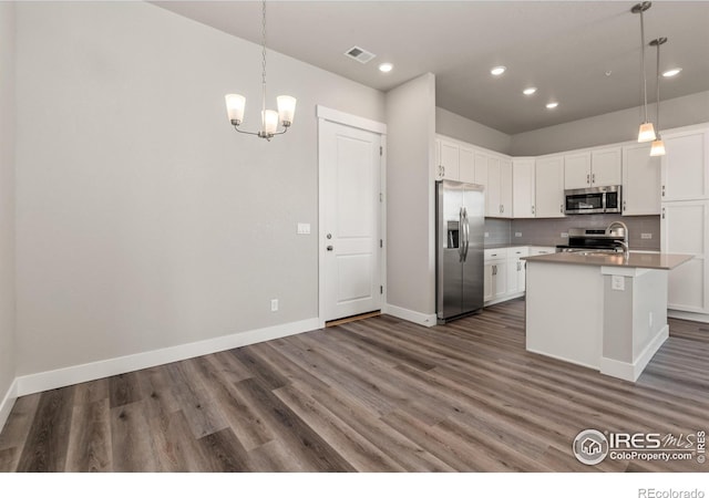 kitchen with appliances with stainless steel finishes, hanging light fixtures, white cabinets, a center island with sink, and dark hardwood / wood-style floors