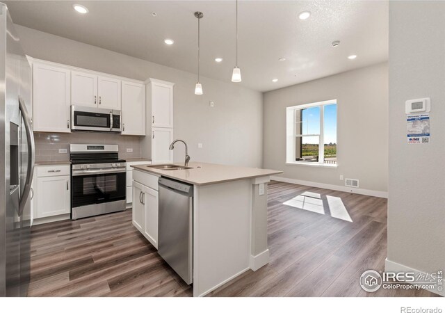 kitchen with white cabinets, stainless steel appliances, decorative light fixtures, a kitchen island with sink, and sink