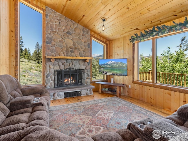 living room with vaulted ceiling, wooden walls, wooden ceiling, wood-type flooring, and a stone fireplace