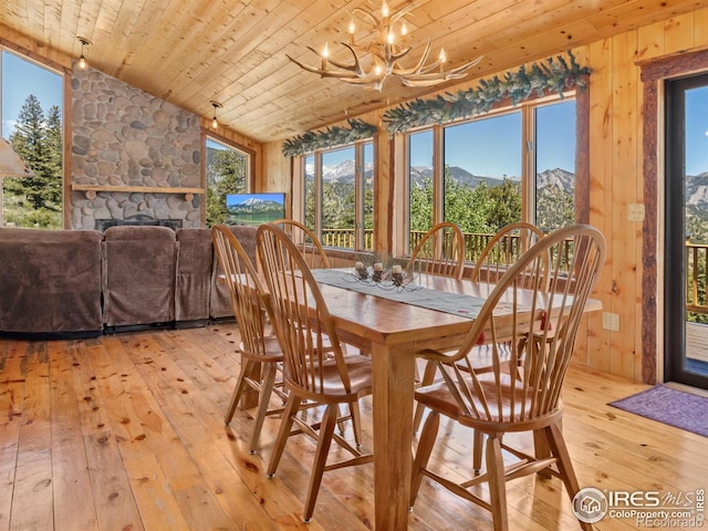 dining space featuring a fireplace, light wood-type flooring, a chandelier, and wood ceiling