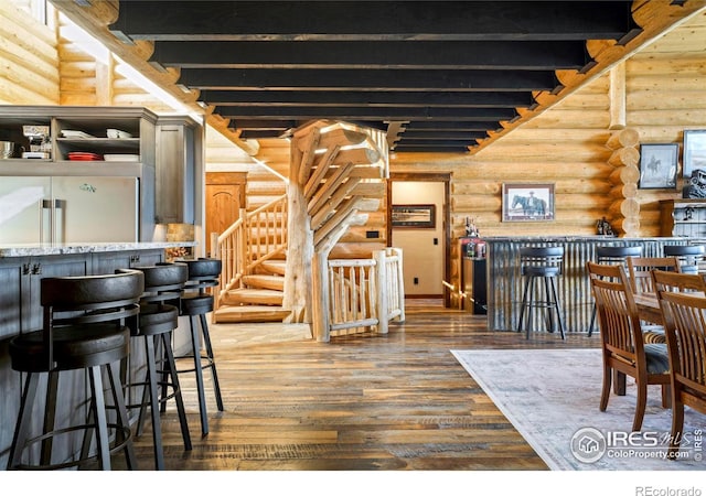 interior space featuring beam ceiling, bar area, log walls, and dark wood-type flooring