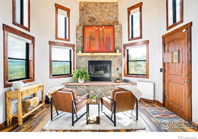 living room with a fireplace, radiator heating unit, a towering ceiling, and hardwood / wood-style flooring