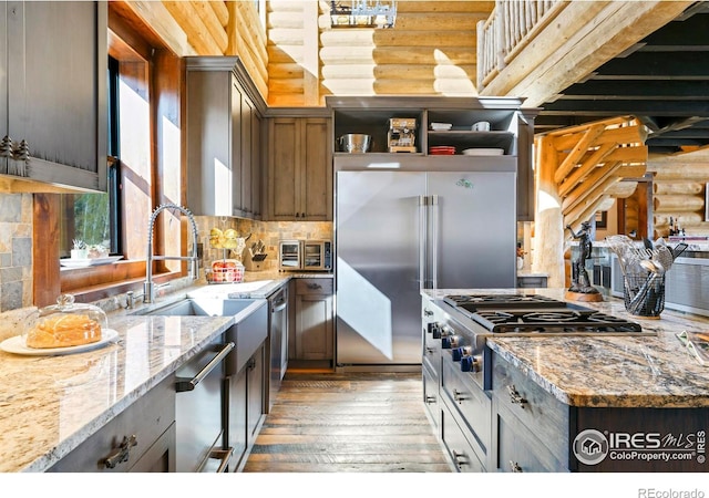 kitchen featuring log walls, stainless steel appliances, light stone counters, light hardwood / wood-style floors, and decorative backsplash