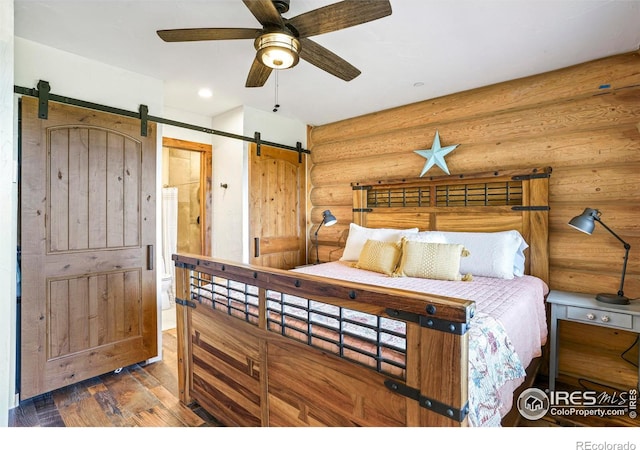 bedroom featuring hardwood / wood-style floors, ceiling fan, a barn door, and log walls