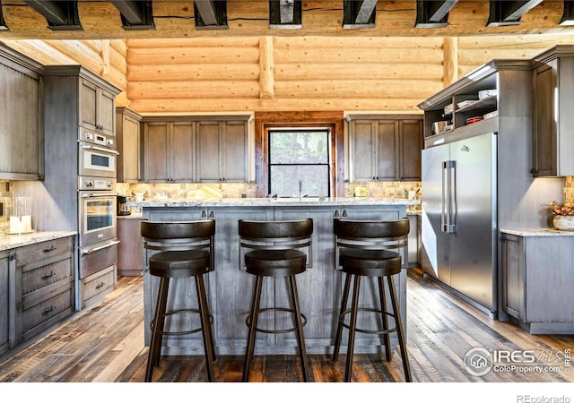 kitchen featuring dark brown cabinetry, light stone countertops, log walls, stainless steel appliances, and dark hardwood / wood-style floors