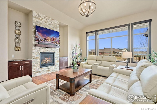 living room featuring a fireplace, light wood-type flooring, an inviting chandelier, and vaulted ceiling