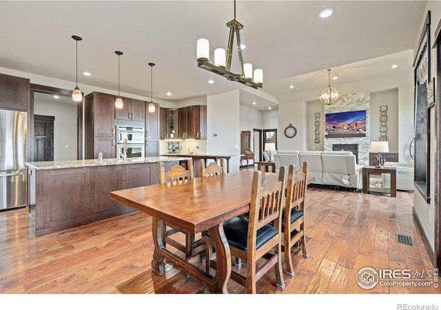 dining area featuring a stone fireplace, light hardwood / wood-style flooring, and a notable chandelier