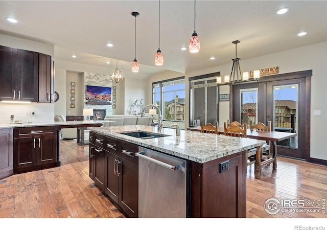 kitchen featuring dishwasher, sink, an island with sink, decorative light fixtures, and light hardwood / wood-style floors