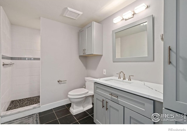 bathroom with toilet, a tile shower, vanity, and tile patterned floors