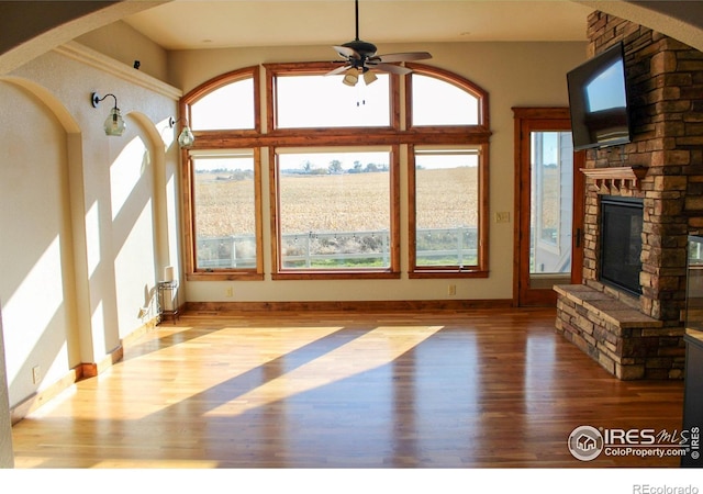 unfurnished living room featuring a stone fireplace, ceiling fan, light hardwood / wood-style flooring, and a healthy amount of sunlight