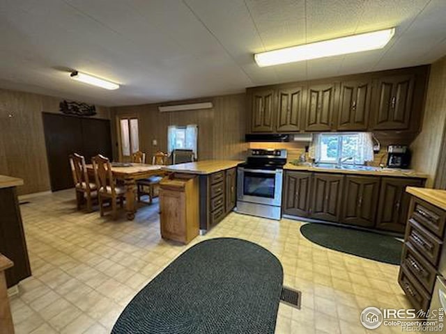 kitchen featuring wooden walls, stainless steel range, exhaust hood, and sink