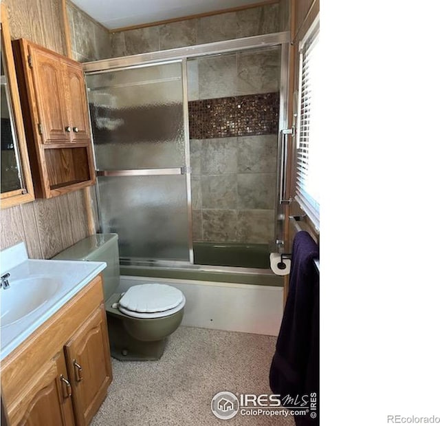 full bathroom with vanity, a healthy amount of sunlight, toilet, and bath / shower combo with glass door