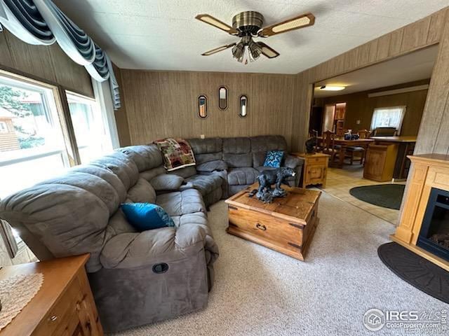 living room featuring a textured ceiling, ceiling fan, light carpet, and wooden walls