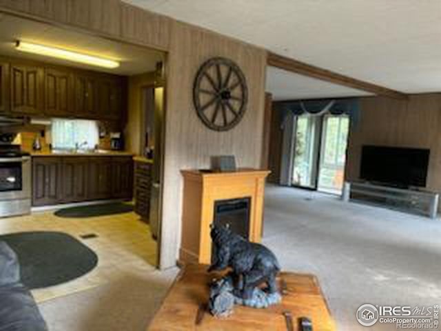 carpeted living room featuring wooden walls and beamed ceiling