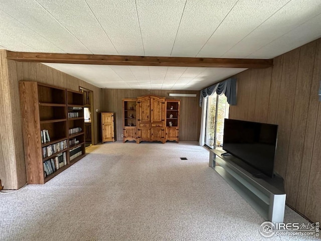 unfurnished living room with carpet, beam ceiling, and wooden walls