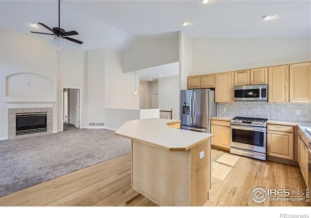 kitchen with light hardwood / wood-style flooring, a tile fireplace, stainless steel appliances, a center island, and tasteful backsplash