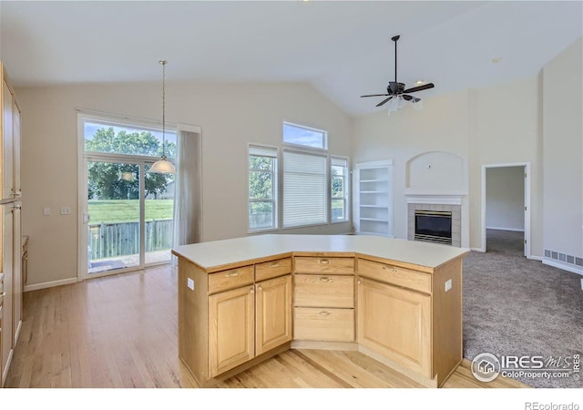 kitchen with a tiled fireplace, decorative light fixtures, light brown cabinetry, and a kitchen island