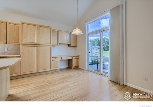 kitchen with light brown cabinetry, decorative light fixtures, built in desk, and light hardwood / wood-style floors