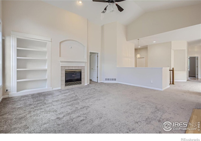 unfurnished living room featuring built in shelves, high vaulted ceiling, ceiling fan, a tile fireplace, and light colored carpet