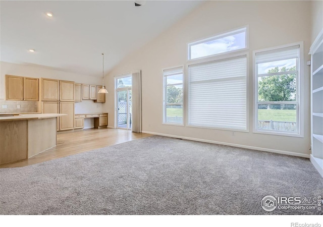 kitchen featuring light brown cabinetry, high vaulted ceiling, decorative light fixtures, and light colored carpet