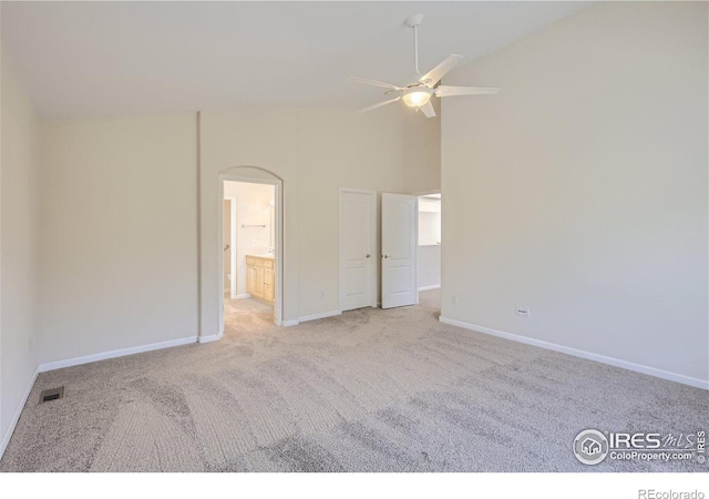 unfurnished bedroom featuring ceiling fan, light colored carpet, high vaulted ceiling, and ensuite bath