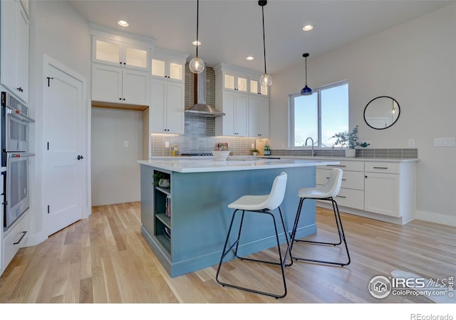 kitchen featuring a center island, white cabinets, wall chimney exhaust hood, decorative light fixtures, and light hardwood / wood-style floors