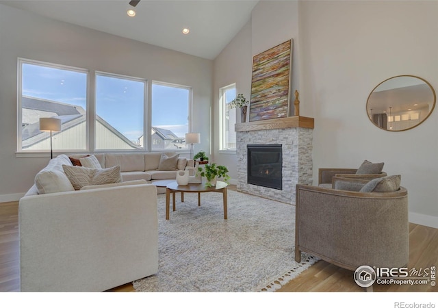 living room with high vaulted ceiling, light hardwood / wood-style floors, and a stone fireplace