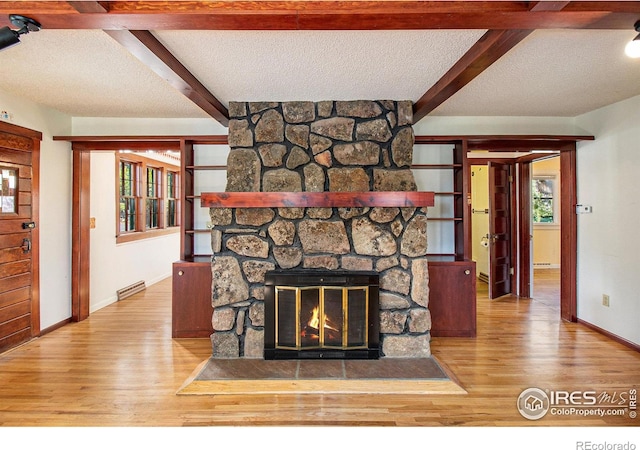 unfurnished living room with beamed ceiling, a textured ceiling, hardwood / wood-style flooring, and a stone fireplace