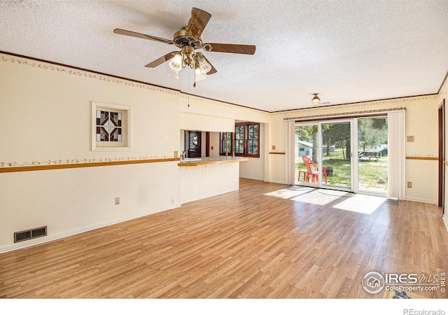 unfurnished living room with ceiling fan, ornamental molding, a textured ceiling, and light hardwood / wood-style flooring