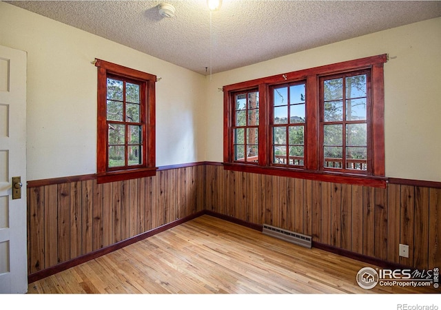 empty room with wood walls, light hardwood / wood-style floors, and a textured ceiling