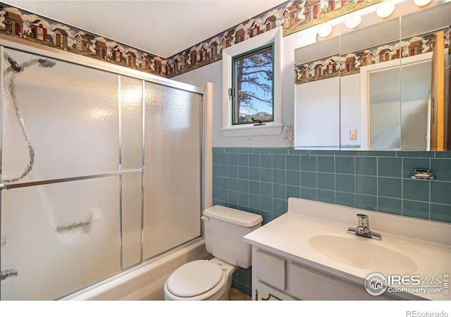 full bathroom featuring combined bath / shower with glass door, vanity, toilet, and tile walls