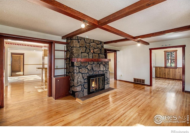 unfurnished living room featuring beam ceiling, a textured ceiling, wooden walls, a fireplace, and hardwood / wood-style flooring