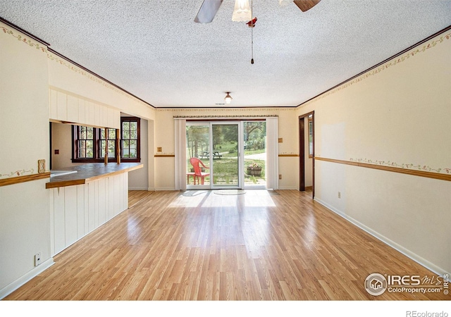 unfurnished living room featuring a textured ceiling, ceiling fan, light wood-type flooring, and ornamental molding