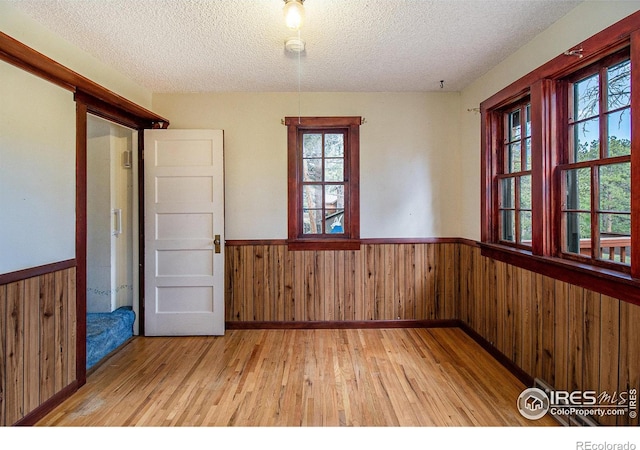 spare room featuring light wood-type flooring, a textured ceiling, and wood walls