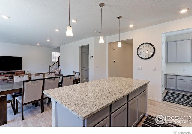 kitchen with light wood-type flooring, light stone counters, gray cabinetry, pendant lighting, and a kitchen island