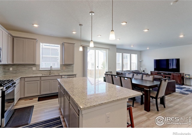 kitchen with gray cabinetry, sink, hanging light fixtures, a kitchen island, and stainless steel range with gas stovetop