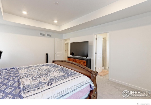 bedroom with a raised ceiling, connected bathroom, and light colored carpet