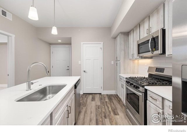 kitchen featuring sink, backsplash, light wood-type flooring, pendant lighting, and stainless steel appliances