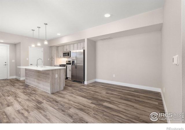 kitchen with appliances with stainless steel finishes, a center island with sink, hanging light fixtures, wood-type flooring, and sink