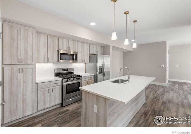 kitchen with an island with sink, stainless steel appliances, sink, dark hardwood / wood-style floors, and pendant lighting