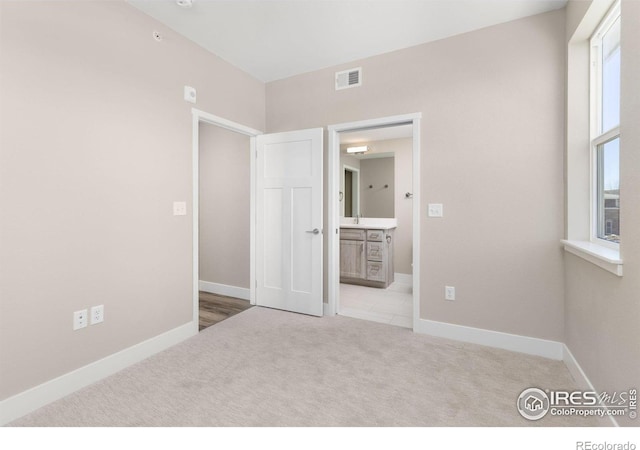 unfurnished bedroom featuring connected bathroom and light colored carpet