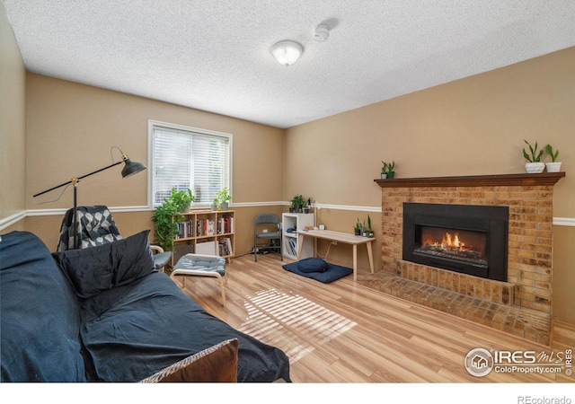 living room featuring a brick fireplace, a textured ceiling, and wood finished floors